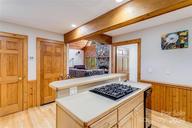 kitchen with black gas cooktop, light hardwood / wood-style flooring, beamed ceiling, light brown cabinetry, and a stone fireplace