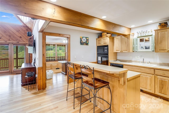 kitchen featuring sink, light wood-type flooring, a kitchen island, a breakfast bar area, and black appliances