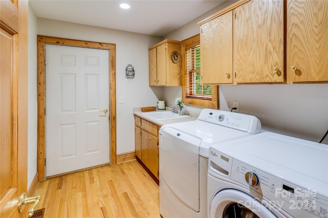 washroom with light hardwood / wood-style floors, sink, washing machine and clothes dryer, and cabinets