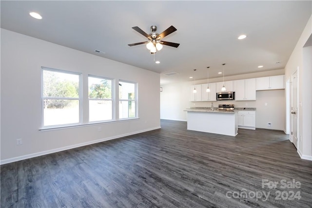 kitchen with pendant lighting, dark wood-type flooring, a center island with sink, white cabinets, and appliances with stainless steel finishes