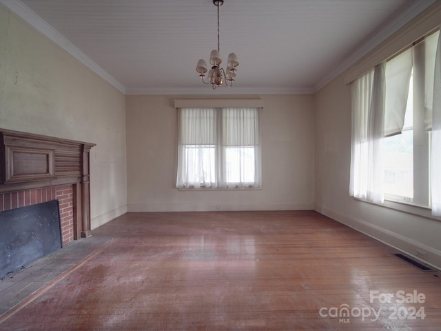 unfurnished living room featuring a notable chandelier, wood finished floors, visible vents, ornamental molding, and a brick fireplace