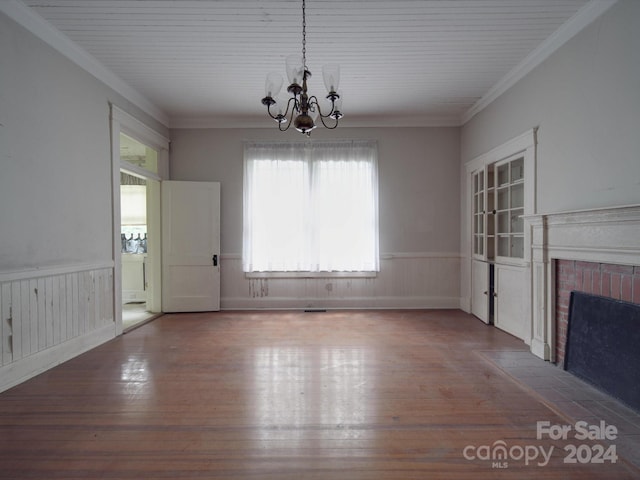 unfurnished dining area with a wainscoted wall, crown molding, a brick fireplace, wood finished floors, and a chandelier