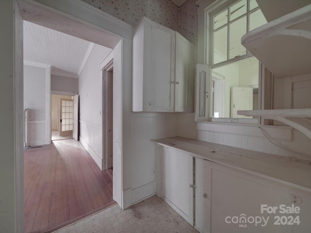 hall featuring wallpapered walls, light floors, and crown molding