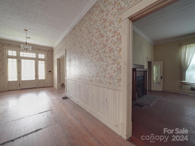 entryway with ornamental molding, wood finished floors, a wainscoted wall, and wallpapered walls