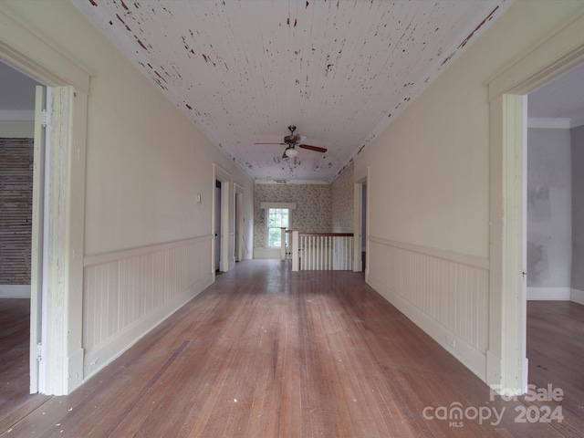 corridor with a wainscoted wall, ornamental molding, and wood finished floors