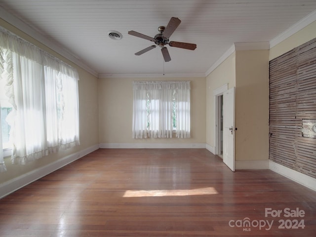 empty room with ornamental molding, visible vents, baseboards, and wood finished floors