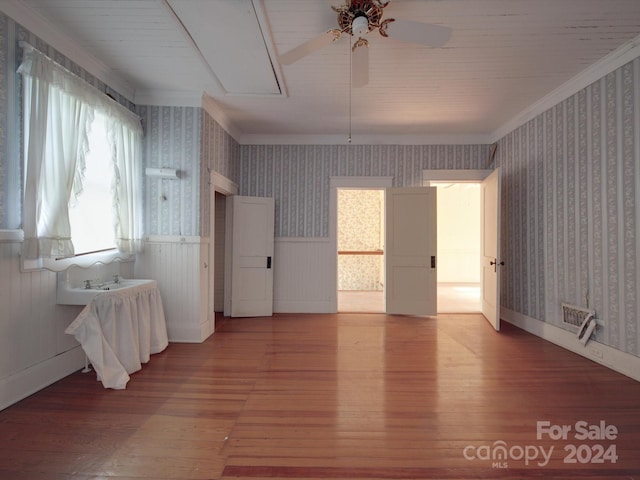 unfurnished room featuring wallpapered walls, attic access, wainscoting, ornamental molding, and wood finished floors