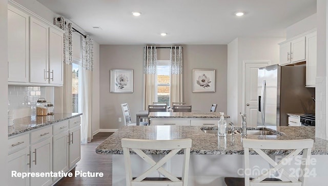 kitchen featuring an island with sink, stainless steel fridge, sink, white cabinets, and a kitchen breakfast bar