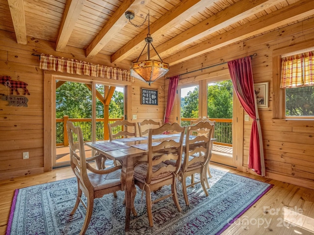 dining space with light hardwood / wood-style flooring, wooden walls, and beam ceiling