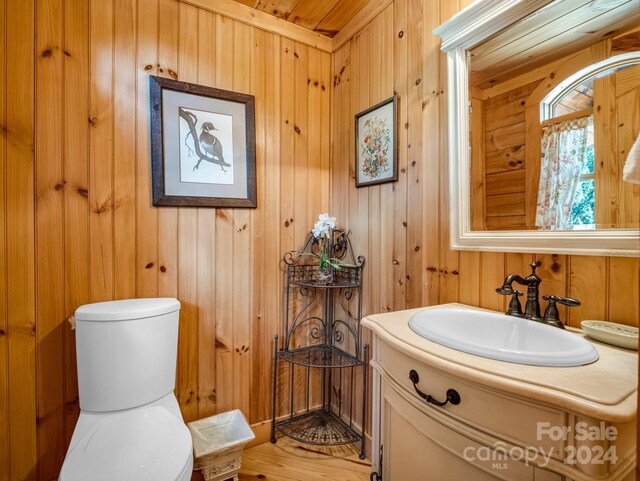 bathroom featuring vanity, toilet, hardwood / wood-style floors, and wooden walls