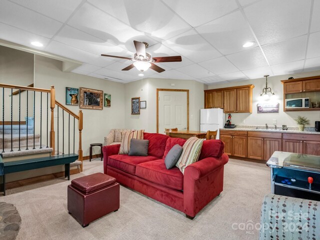 carpeted living room with a paneled ceiling, ceiling fan, and sink