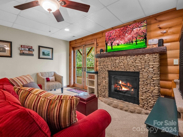 carpeted living room featuring a fireplace, log walls, a drop ceiling, and a ceiling fan