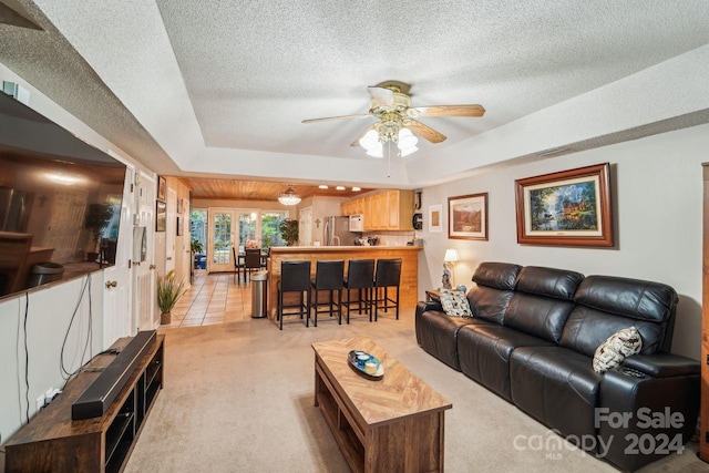 living room featuring ceiling fan, a textured ceiling, light carpet, and a tray ceiling