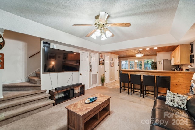 living room with light colored carpet, a textured ceiling, a raised ceiling, and ceiling fan