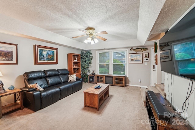 carpeted living room with a textured ceiling, a tray ceiling, and ceiling fan