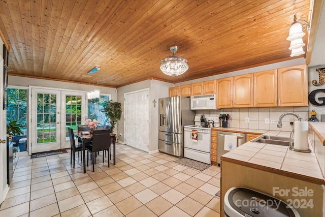 kitchen featuring appliances with stainless steel finishes, decorative backsplash, sink, tile countertops, and hanging light fixtures