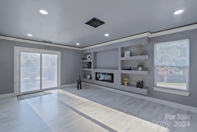 living room featuring built in shelves, light hardwood / wood-style floors, a healthy amount of sunlight, and ornamental molding