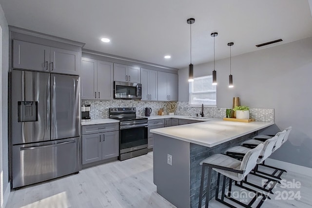 kitchen with appliances with stainless steel finishes, a breakfast bar area, a peninsula, light countertops, and pendant lighting