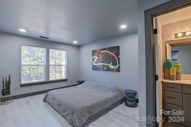 bedroom with a textured ceiling, light hardwood / wood-style floors, and ensuite bathroom