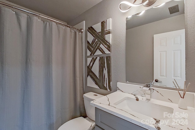 bathroom featuring a textured wall, vanity, and toilet