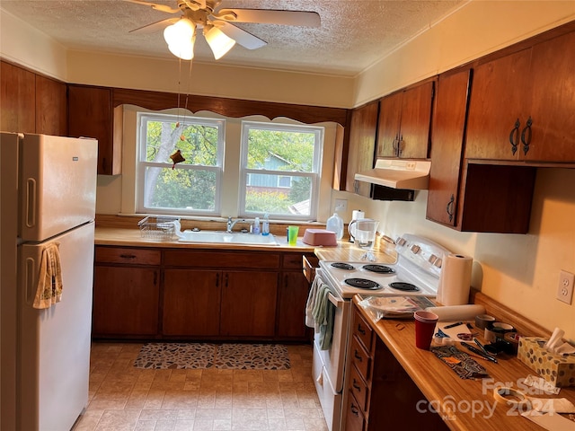 kitchen featuring white appliances, light countertops, a textured ceiling, under cabinet range hood, and a sink