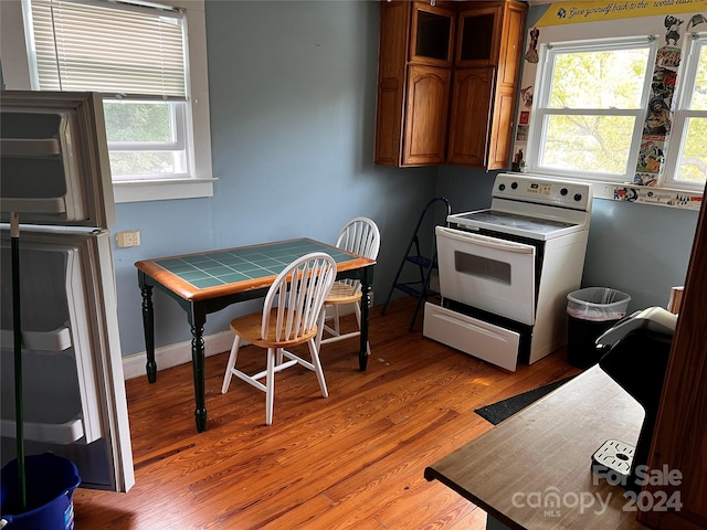 kitchen featuring light wood-type flooring, brown cabinets, baseboards, and white range with electric cooktop