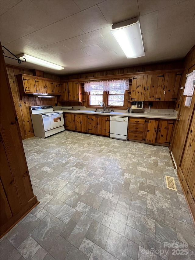 kitchen featuring white appliances, sink, and wooden walls