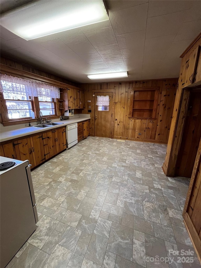 kitchen featuring dishwasher, stove, wooden walls, and sink