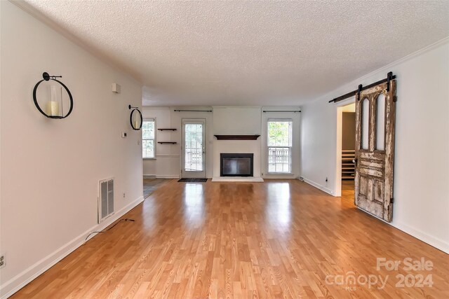 unfurnished living room with a textured ceiling, plenty of natural light, a barn door, and light hardwood / wood-style flooring