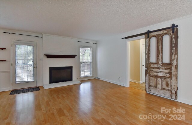 unfurnished living room featuring plenty of natural light, a brick fireplace, wood-type flooring, and a barn door