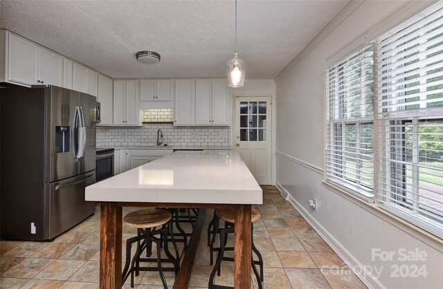 kitchen with backsplash, stainless steel appliances, white cabinetry, sink, and pendant lighting