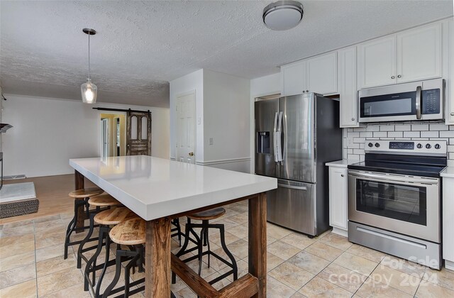 kitchen featuring a textured ceiling, pendant lighting, backsplash, stainless steel appliances, and white cabinets