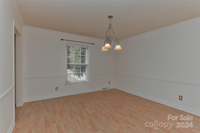 empty room featuring a chandelier and light hardwood / wood-style floors