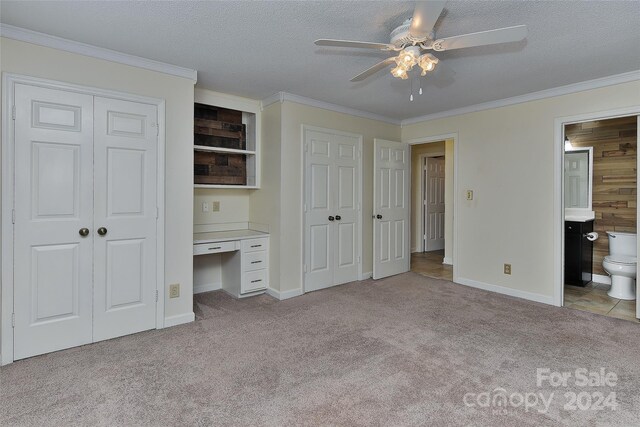 unfurnished bedroom featuring ensuite bath, light colored carpet, ceiling fan, and wooden walls