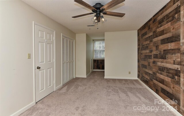 empty room with ceiling fan, wooden walls, light carpet, and a textured ceiling