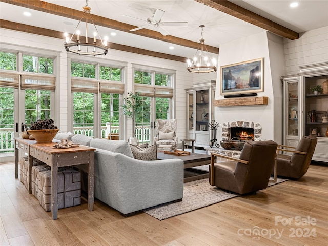 living room with ceiling fan with notable chandelier, light hardwood / wood-style flooring, a large fireplace, and beam ceiling