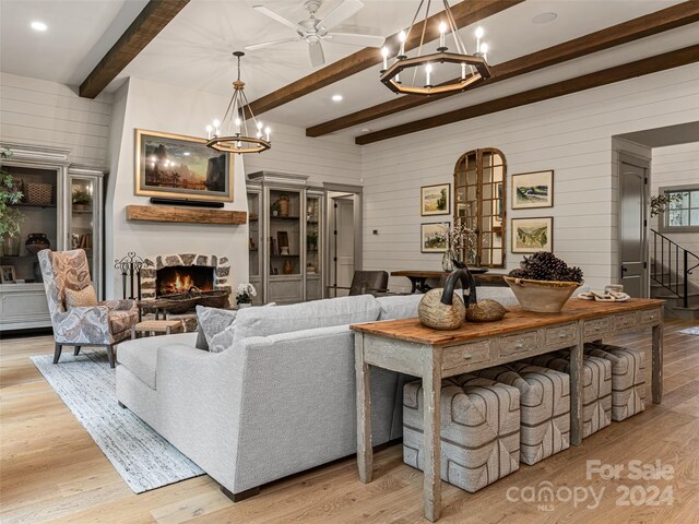 living room featuring light hardwood / wood-style floors, a large fireplace, ceiling fan with notable chandelier, and beamed ceiling