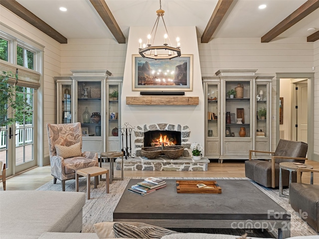 living room with a stone fireplace, wood walls, a chandelier, and light wood-type flooring