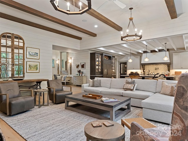 living room with ornate columns, an inviting chandelier, beamed ceiling, and light wood-type flooring