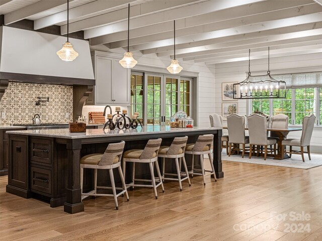 kitchen featuring light hardwood / wood-style floors, a breakfast bar, beamed ceiling, and dark brown cabinets