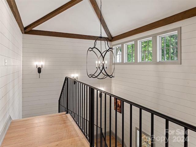 staircase featuring wood walls, a notable chandelier, hardwood / wood-style floors, and lofted ceiling with beams