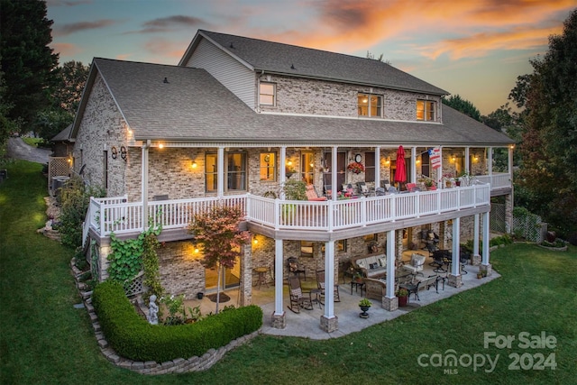 rear view of property featuring a patio area, stone siding, a lawn, and roof with shingles