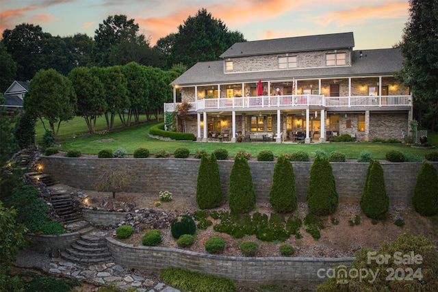 rear view of property featuring a patio, a lawn, and stone siding