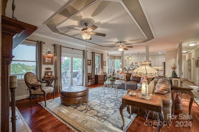 living area featuring a ceiling fan, wood finished floors, baseboards, decorative columns, and crown molding