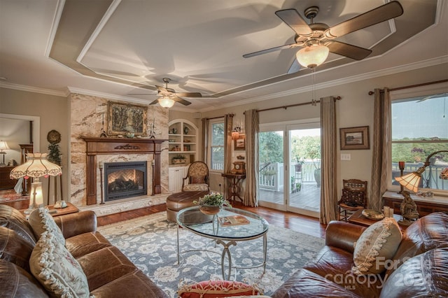 living area with ceiling fan, built in features, a premium fireplace, ornamental molding, and wood finished floors