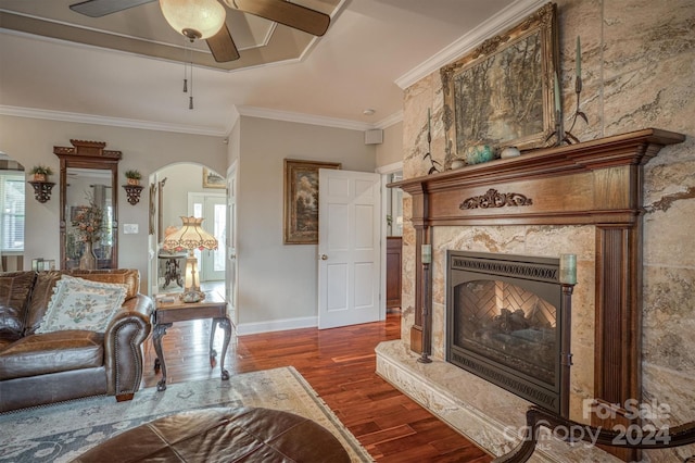 living room with crown molding, a fireplace, ceiling fan, and dark wood-type flooring