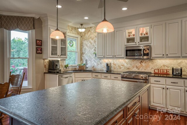 kitchen featuring ornamental molding, a sink, dark countertops, stainless steel appliances, and glass insert cabinets