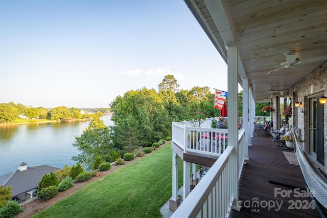 deck featuring a water view, ceiling fan, and a lawn