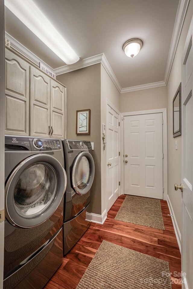 laundry room featuring washer and clothes dryer, cabinets, ornamental molding, and dark wood-type flooring