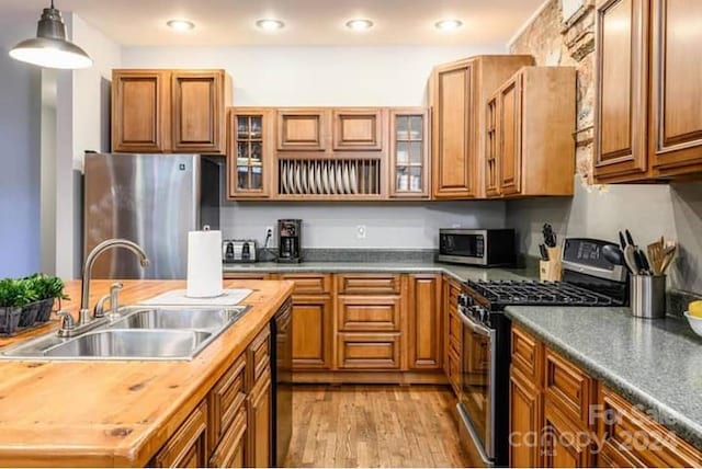 kitchen with hanging light fixtures, light hardwood / wood-style flooring, butcher block counters, sink, and stainless steel appliances